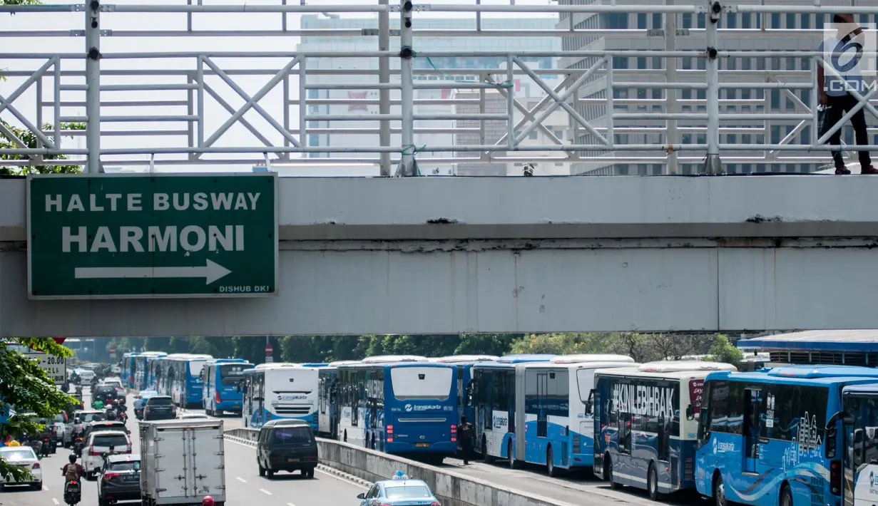 Seorang warga berdiri diatas jembatan penyebrangan di dekat jejeran bus Tranjakarta yang mogok kerja di Halte Harmoni, Jakarta (12/6). Supir beserta karyawan Transjakarta menuangkan tuntutan tersebut dalam petisi. (Liputan6.com/Gempur M Surya)