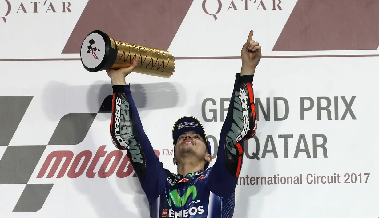 Pembalap Movistar Yamaha MotoGP, Maverick Vinales, mengangkat pialanya di atas podium setelah memenangi MotoGP Qatar di Sirkuit Losail, Doha, Minggu (26/3). Vinales menyelesaikan balapan dengan catatan waktu 38 menit 59,999 detik. (Karim JAAFAR/AFP)