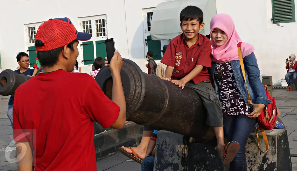 Warga berfoto diatas meriam kuno di kawasan Kota Tua, Jakarta, Minggu (8/5). Di hari terakhir libur panjang, kawasan Kota Tua masih menjadi lokasi favorit warga untuk berwisata dengan biaya yang terjangkau. (Liputan6.com/Immanuel Antonius)