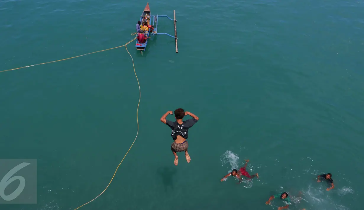 Aksi seorang anak ketika melompat ke laut untuk memburu koin yang dilemparkan penumpang dari atas kapal di Pelabuhan Merak, Banten, Jumat (26/8). Aksi itu menjadi hiburan bagi penumpang yang akan menyeberang ke Pulau Sumatera. (Liputan6.com/Angga Yuniar)