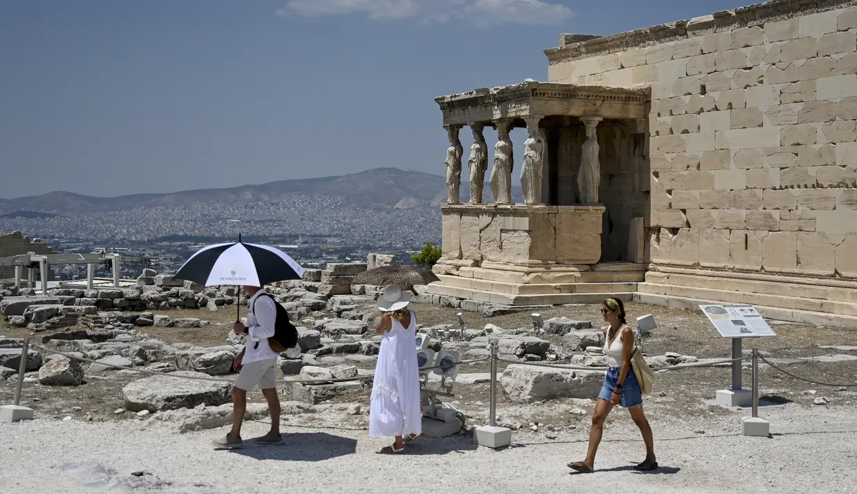 <p>Turis menggunakan payung untuk melindungi diri dari sinar matahari saat mengunjungi Acropolis di Athena, Yunani, Minggu (24/7/2022). Negara ini berada dalam cengkeraman gelombang panas yang dimulai pada 23 Juli dan akan berlangsung beberapa hari. Suhu diperkirakan akan mencapai 42 derajat Celcius (107 derajat Fahrenheit) di beberapa daerah. (Louisa GOULIAMAKI / AFP)</p>