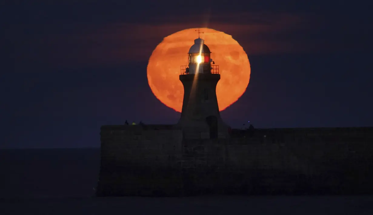 Bulan purnama yang dikenal sebagai Harvest moon muncul di atas mercusuar South Shields di pantai timur laut Inggris, Senin (20/9/2021). Ahli bulan NASA, Gordon Johnston, menerangkan harvest moon adalah bulan purnama yang paling dekat dengan titik balik musim gugur. (Owen Humphreys/PA via AP)