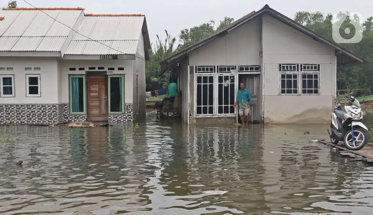 Seorang warga berdiri di depan rumahnya yang tergenang banjir rob di Desa Pantai Mekar, Muaragembong, Kabupaten Bekasi, Senin (6/12/2021). Banjir rob telah menggenangi rumah dan tambak warga di wilayah tersebut selama empat hari akibat kenaikan permukaan air laut. (Liputan6.com/Herman Zakharia)