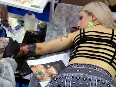 Seorang wanita terbaring saat membuat tato wajah menyerupai gambar seorang anak di tangannya selama acara Tattoo Week SP 2016 di Sao Paulo, Brasil, (23/7). (REUTERS/Paulo Whitaker)