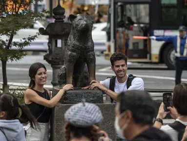 Pasangan berpose untuk berfoto di samping patung "Hachiko" di depan stasiun Shibuya di pusat kota Tokyo menjelang peringatan 100 tahun kelahiran anjing legendaris tersebut bulan ini pada 6 November 2023. (Richard A. Brooks / AFP)