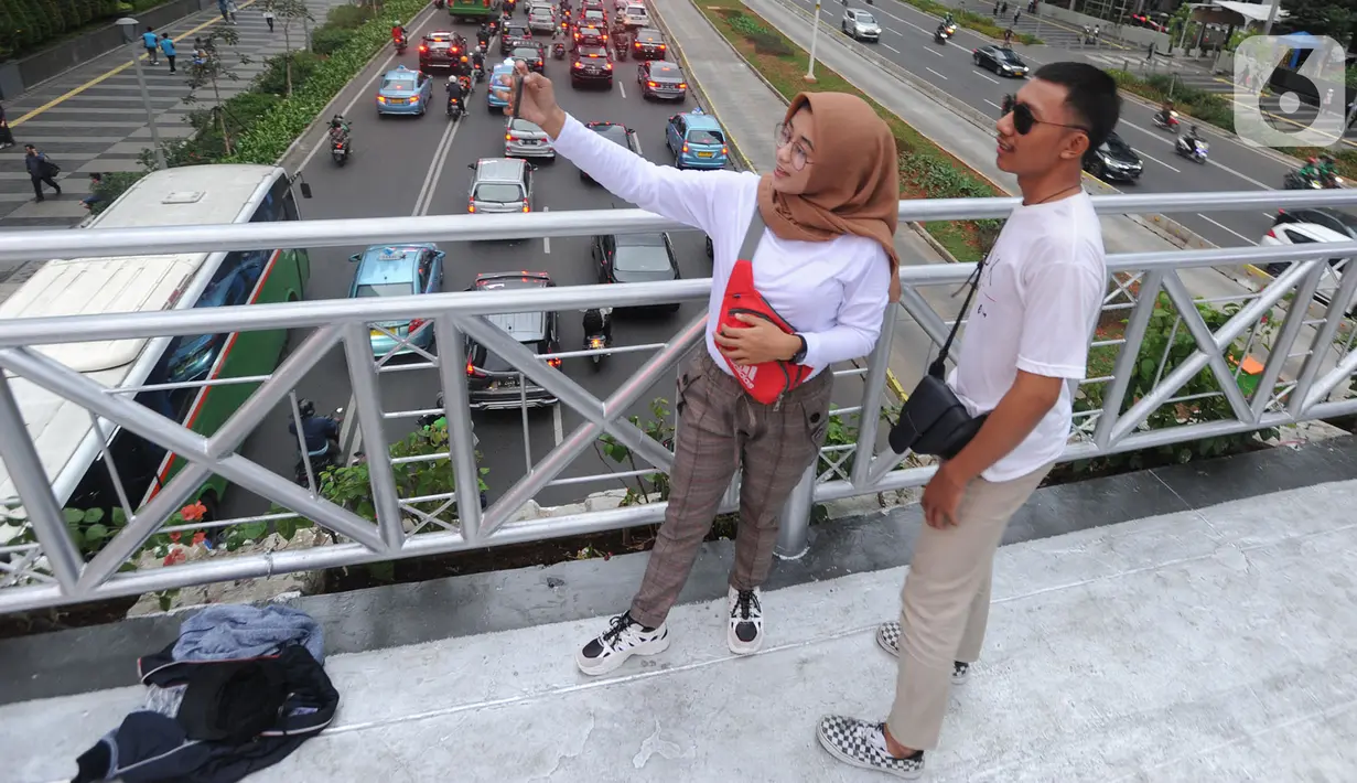 Pejalan kaki berswafoto di jembatan penyeberangan orang (JPO) yang tidak beratap di jalan Sudirman, Jakarta, Rabu (6/11/2019). Pemprov DKI mengklaim mayoritas masyarakat Jakarta setuju dengan konsep JPO terbuka dan tanpa atap yang kini dibangun di Sudirman. (merdeka.com/Arie Basuki)