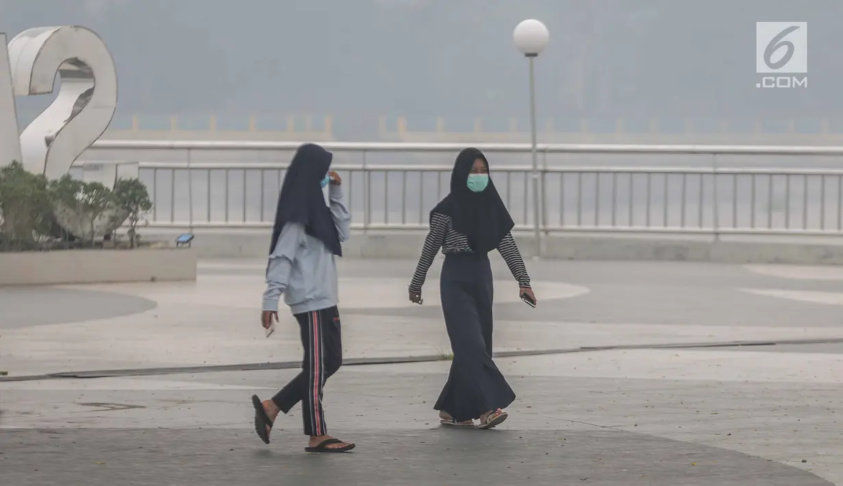 Dua wanita mengenakan masker saat mengunjungi alun-alun Kabupaten Siak, Riau, Kamis (12/9/2019). Asap pekat kebakaran lahan gambut tersebut selain mengganggu kesehatan serta mencemari udara sehingga kualitasnya turun ke status tidak sehat. (Liputan6.com/Faizal Fanani)