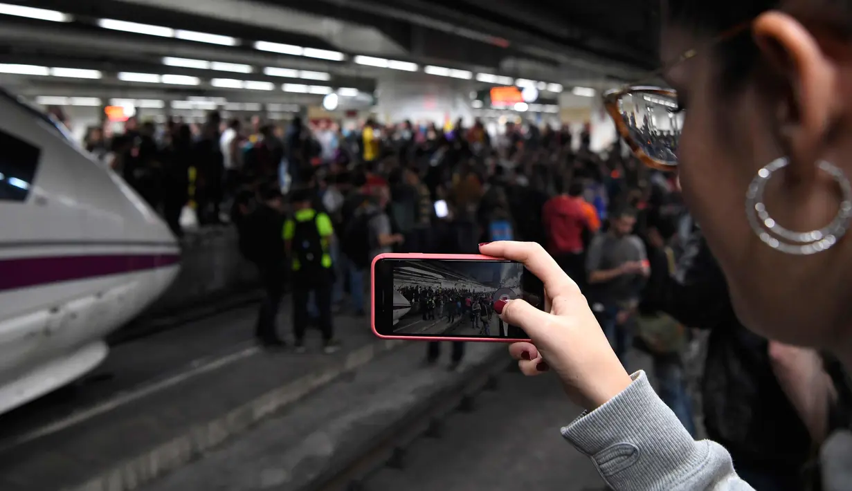 Seorang wanita mengabadikan gambar saat para pengunjuk rasa memblokir rel kereta api di Stasiun Sants di Barcelona (8/11). Pengunjuk rasa memblokir jalan dan jalur kereta api setelah para pemimpin separatis ditahan di Madrid. (AFP Photo/Lluis Gene)