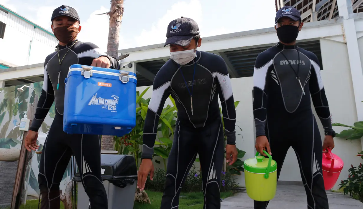 Pelatih mengenakan masker saat mereka membawa wadah untuk memberi makan lumba-lumba di sebuah pusat konservasi di Bali, Selasa (28/4/2020). Semua tempat wisata dan situs telah diminta untuk sementara waktu ditutup sebagai langkah untuk mengendalikan penyebaran Covid-19. (AP Photo/Firdia Lisnawati)