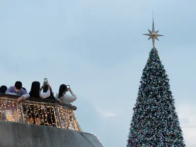 Orang-orang mengambil foto pohon Natal raksasa selama Natal di distrik budaya West Kowloon di Hong Kong (25/12/2021). Pohon Natal raksasa didekorasi secara glamor dengan karangan bunga dan ornamen, berkilauan dengan lampu meriah yang cerah. (AFP/Bertha Wang)