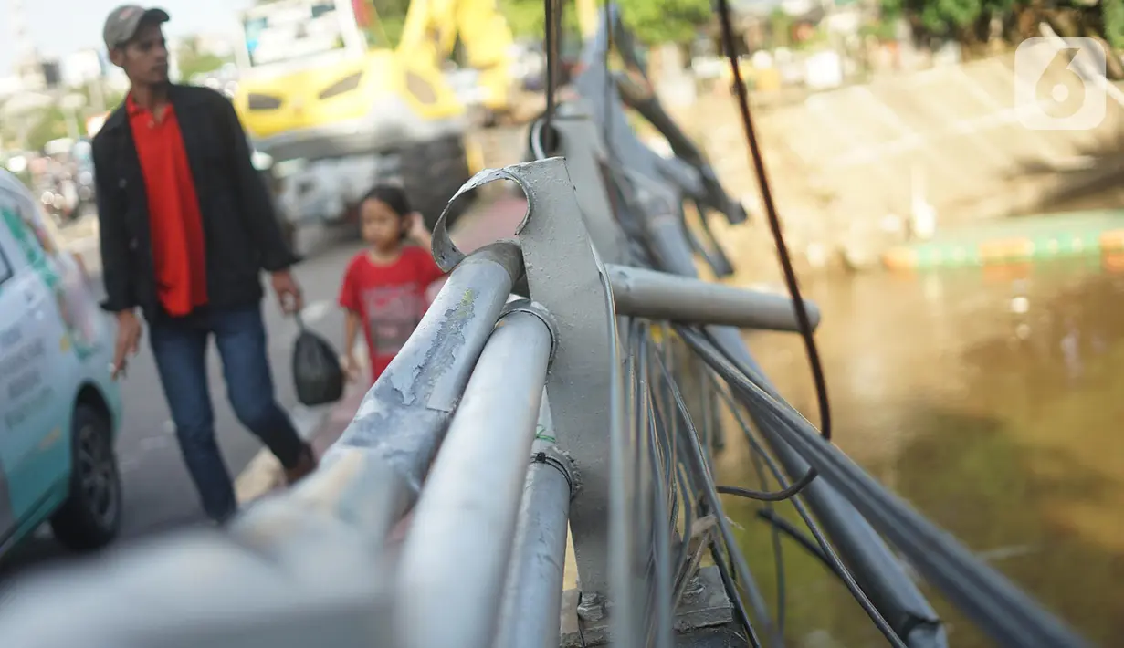 Warga berjalan di samping pagar jembatan yang rusak di kawasan Bukit Duri, Jakarta, Jumat (21/2/2020). Pagar yang rusak akibat penanganan sampah banjir tersebut hingga kini belum juga diperbaiki. (Liputan6.com/Immanuel Antonius)