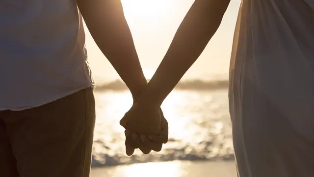 Sepasang kekasih bergandengan tangan di sebuah pantai dengan matahari terbenam (Foto Dok: Freepik/wavebreakmedia_micro)