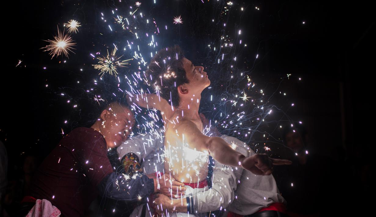 Seorang pria bermandinkan percikan kembang api saat mengikuti ritual eating flowers di provinsi Fujians, China (16/2). Ritual unik ini digelar untuk mengusir roh-roh jahat. (AFP/Johannes Eisele)
