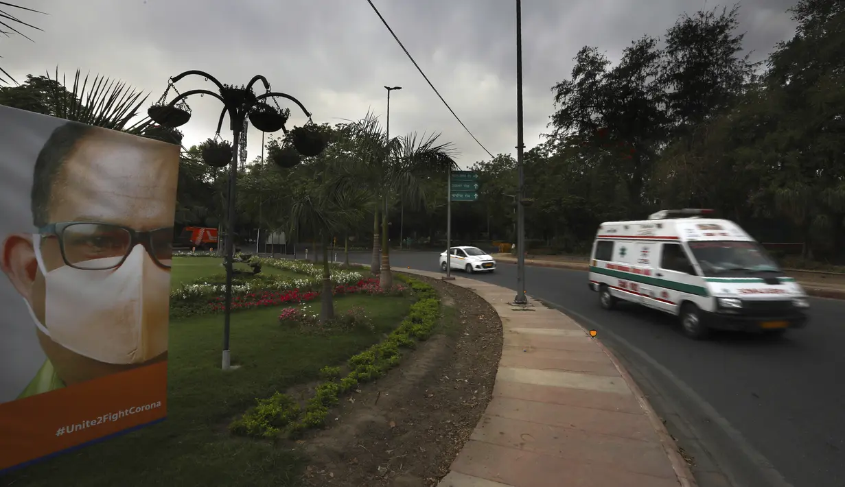 Sebuah ambulans yang membawa pasien melewati poster kesadaran virus Corona di jalan sepi pada hari pertama lockdown diberlakukan di ibu kota India, New Delhi, Selasa (20/4/2021). India melaporkan 259.170 infeksi baru dan 1.761 kematian akibat Covid-19 dalam 24 jam terakhir. (AP Photo/Manish Swarup)