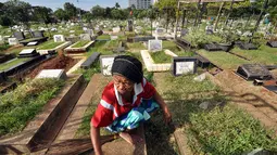 Seorang pengurus makam membersihkan salah satu kuburan yang mulai ditumbuhi rumput liar di TPU Karet Bivak, Jakarta, Minggu (11/1/2015). (Liputan6.com/Miftahul Hayat)