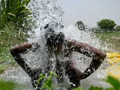 Seorang pria mandi di bawah air yang mengalir dari pipa di sepanjang dataran Yamuna pada suatu sore di New Delhi pada tanggal 29 Mei 2024. (Arun SANKAR/AFP)