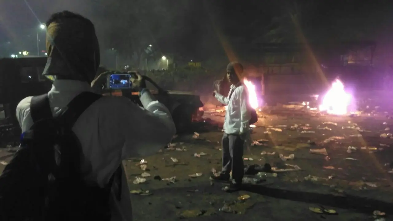 Selfie di depan mobil aparat yang terbakar