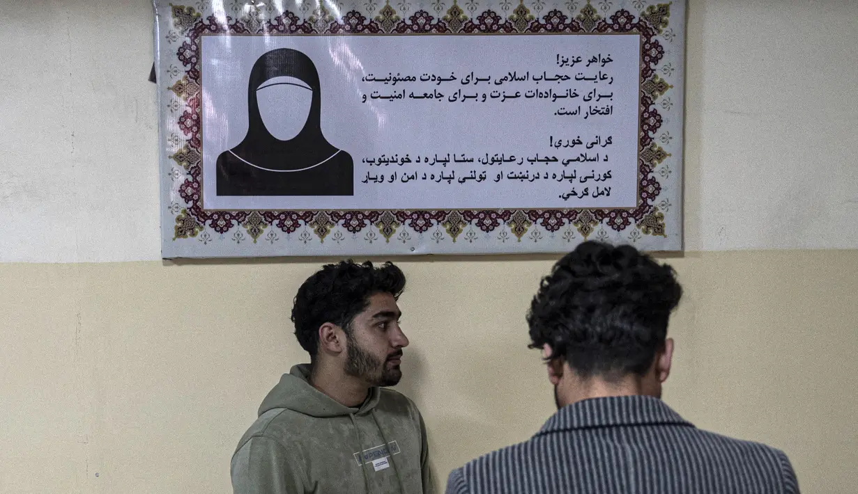 Mahasiswa berdiri di depan poster yang memerintahkan perempuan menutup diri dengan Jilbab, di koridor sebuah universitas swasta setelah universitas dibuka kembali di Kabul, Afghanistan, Senin (6/3/2023). Pemerintah Taliban memberlakukan larangan perempuan untuk kembali ke kelas setelah menuduh mahasiswi mengabaikan aturan berpakaian yang ketat dan persyaratan untuk ditemani kerabat laki-laki ke dan dari kampus. (Wakil KOHSAR / AFP)