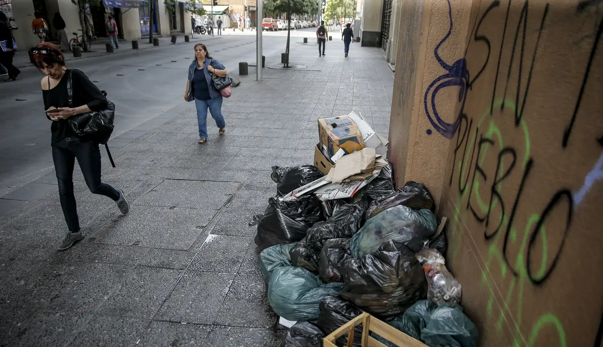 Orang-orang berjalan melewati tumpukan sampah yang diakibatkan pemogokan petugas sampah di Santiago (14/11/2019). Protes kekerasan meletus di ibukota Chile, Santiago, pada Selasa ketika mata uang negara itu turun ke level terendah dalam sejarah. (AFP/Javier Torres)