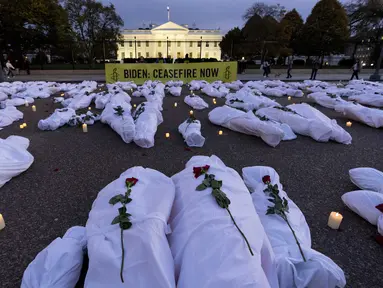 Spanduk besar bertuliskan "Biden: Gencatan Senjata Sekarang" bersama dengan kantong mayat palsu berwarna putih, dipajang di depan Gedung Putih pada senja, di Washington, Rabu (15/11/2023). (AP Photo/Andrew Harnik)