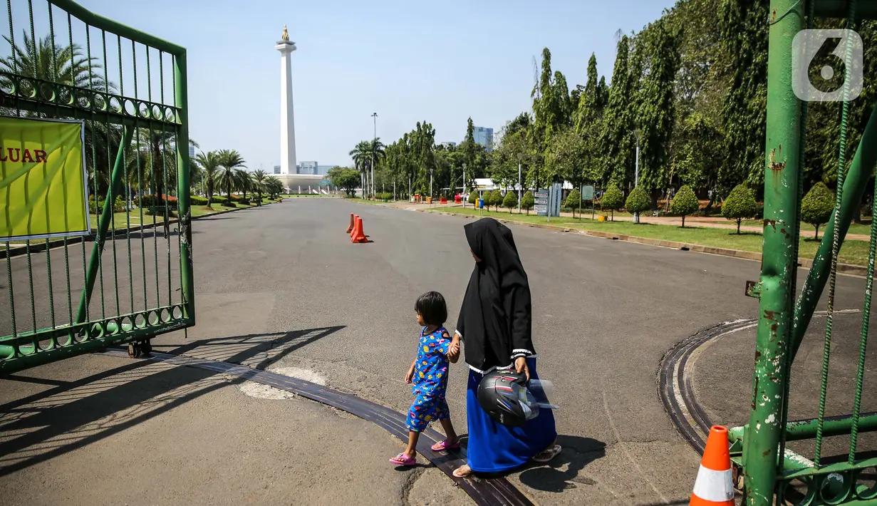 Sejumlah warga berjalan di depan kawasan Monumen Nasional (Monas), Jakarta, Minggu (26/7/2020). Sejumlah warga mulai mengunjungi kawasan Monas meski masih ditutup sementara di masa PSBB transisi. (Liputan6.com/Faizal Fanani)
