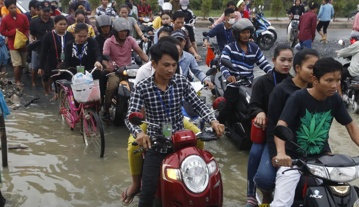 Pekerja garmen pergi ke tempat kerja melalui jalan yang banjir setelah hujan di  Phnom Penh, Kamboja (14 /10/2020). Pejabat bencana Kamboja mengatakan bahwa lebih dari 10.000 orang telah dievakuasi ke tempat aman setelah badai tropis melanda yang menyebabkan banjir bandang.  (AP Photo/Heng Sinith)