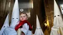 Seorang anggota persaudaraan "La Borriquita" menggedong anaknya saat mengikuti pengakuan dosa dalam acara prosesi Pekan Suci di Cordoba, Spanyol (9/4). (AP Photo / Manu Fernandez)