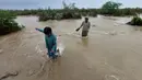 Penduduk desa melintasi daerah banjir untuk pindah ke tempat yang lebih tinggi setelah hujan lebat, di Lasbella, sebuah distrik di provinsi Baluchistan barat daya Pakistan (26/7/2022). Para pejabat mengatakan, pada hari Rabu, penyelamat yang didukung oleh pasukan menggunakan perahu dan helikopter untuk mengungsi ratusan orang terdampar dari barat daya Pakistan, di mana banjir yang dipicu oleh hujan telah menewaskan 104 orang sejak bulan lalu. (AP Photo/Hamdan Khan)