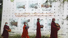 Biksu Buddha mengenakan masker berjalan melewati papan peringatan COVID-19 saat mereka mengumpulkan sedekah pagi di Yangon, Myanmar, Kamis (15/7/2021). Hampir 90 persen wilayah di Myanmar telah terkena dampak gelombang ketiga Covid-19. (AP Photo/Thein Zaw)
