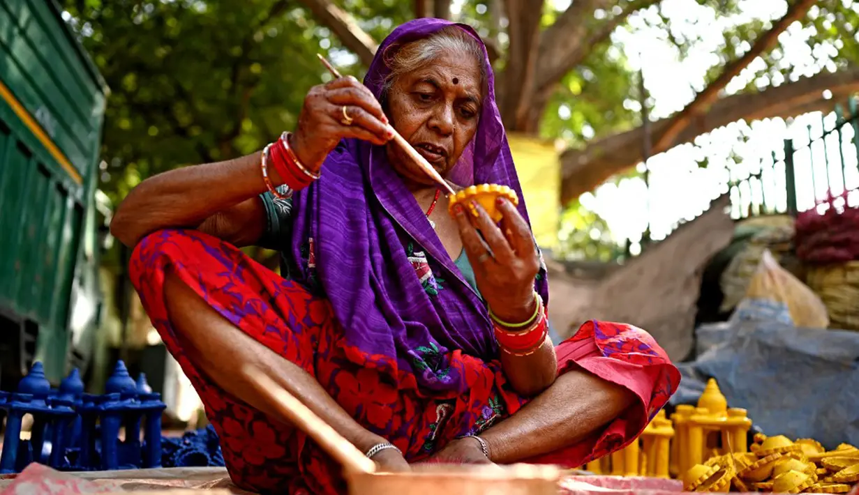 Seorang pembuat tembikar melukis lampu tanah jelang Festival Diwali di sepanjang pinggir jalan di New Delhi, India, 18 Oktober 2022. Festival Diwali atau dalam agama Hindu berarti Festival Cahaya melambangkan kemenangan baik atas keburukan, dan lampu atau pelita dinyalakan sebagai tanda perayaan serta harapan umat manusia. (Sajjad HUSSAIN/AFP)