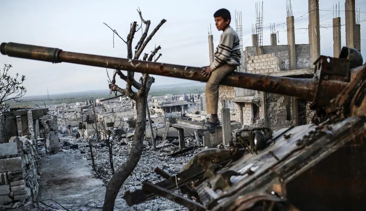 Seorang anak laki-laki Kurdi duduk di atas tank yang hancur di Kota Kobane  yang juga dikenal sebagai Ain al-Arab, Suriah, 26 Maret 2015. (Photo by YASIN AKGUL/AFP)