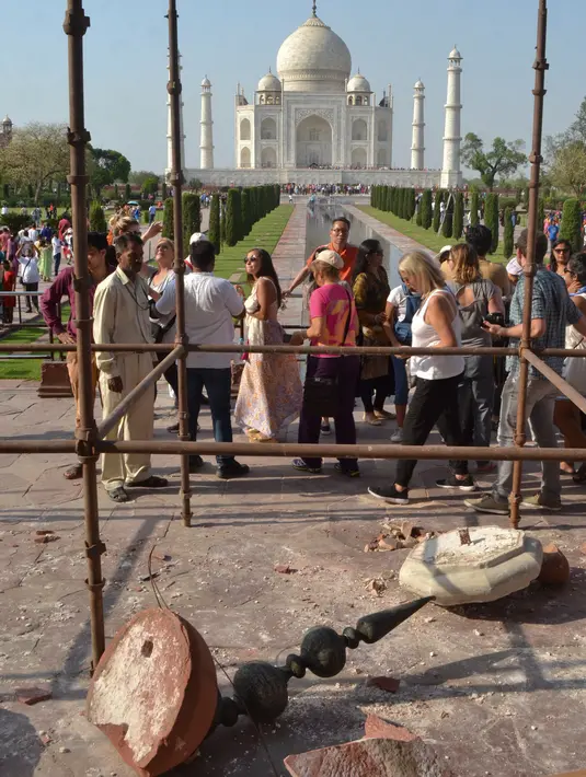 Turis melewati reruntuhan puing-puing pilar Taj Mahal yang roboh di pintu masuk bangunan ikonik tersebut di Agra, India, Kamis (12/4). Angin kencang dengan kecepatan 130 kilometer per jam menyebabkan pilar setinggi 4 meter itu runtuh. (AP/Pawan Sharma)