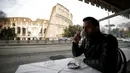 Seorang pria minum kopi di depan Colosseum yang kembali dibuka, Roma, Italia, Senin (1/2/2021). Italia mencabut sebagian langkah pembatasan yang bertujuan untuk menahan penyebaran COVID-19 pada 1 Februari 2021. (Cecilia Fabiano/LaPresse via AP)