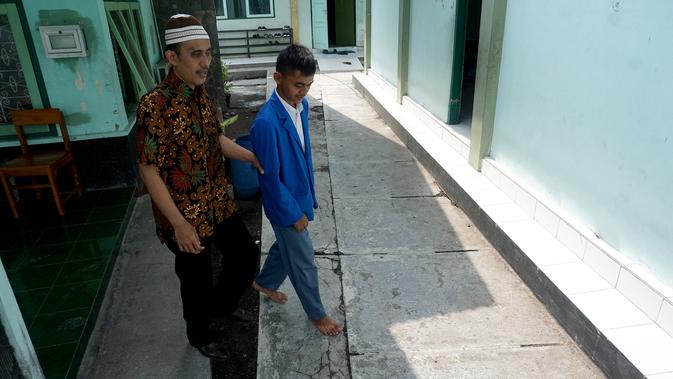 Rasino, guru penyandang tuna netra sedang dituntun muridnya menuju ruang praktik jurusan perdalangan di SMKN 8 Surakarta.(Liputan6com/Fajar Abrori)