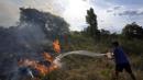 Seorang warga mencoba menyiram padang rumput yang terbakar selama kebakaran semak di lingkungan Banco San Miguel di Asuncion, Paraguay (18/1/2022). Cuaca kering yang tidak biasa memicu kebakaran di ladang terbuka, peternakan pribadi, dan lahan publik di sekitar kota. (AP Photo/Jorge Saenz)