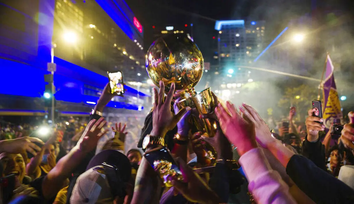 Tangan para fans LA Lakers berusaha menggapai trofi saat merayakan gelar juara NBA 2020 di Los Angeles, Senin (12/10/2020). LA Lakers menjuara NBA 2020 setelah mengalahkan Miami Heat dengan skor 106-93 dalam final gim ke enam. (AP Photo/Jintak Han)