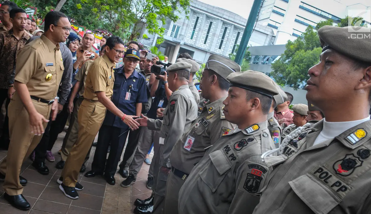 Gubernur dan Wakil Gubernur baru DKI, Anies Baswedan dan Sandiaga Uno menyapa Satpol PP yang sedang apel setibanya di Balai Kota Jakarta, Selasa (17/10). Anies dan Sandiaga keliling Balai Kota pada hari pertama mereka bertugas (Liputan6.com/Faizal Fanani)