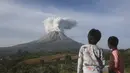 Dua orang Anak menyaksikan Gunung Sinabung memuntahkan material vulkanik saat meletus di Karo, Sumatera Utara, Kamis (11/3/2021). Gunung berapi tersebut mengeluarkan longsoran awan gas membakar yang mengalir menuruni lerengnya saat terjadi letusan pada hari Kamis. (AP Photo/Binsar Bakkara)