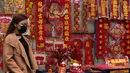 Seorang wanita berjalan melewati catatan berisi kaligrafi dan dekorasi Tahun Baru Imlek yang dipajang untuk dijual di jalan untuk merayakan Tahun Baru Imlek di Hong Kong (14/1/2022). Penangguhan tersebut bertujuan untuk mencegah penyebaran virus corona varian Omicron. (AP Photo/Kin Cheung)