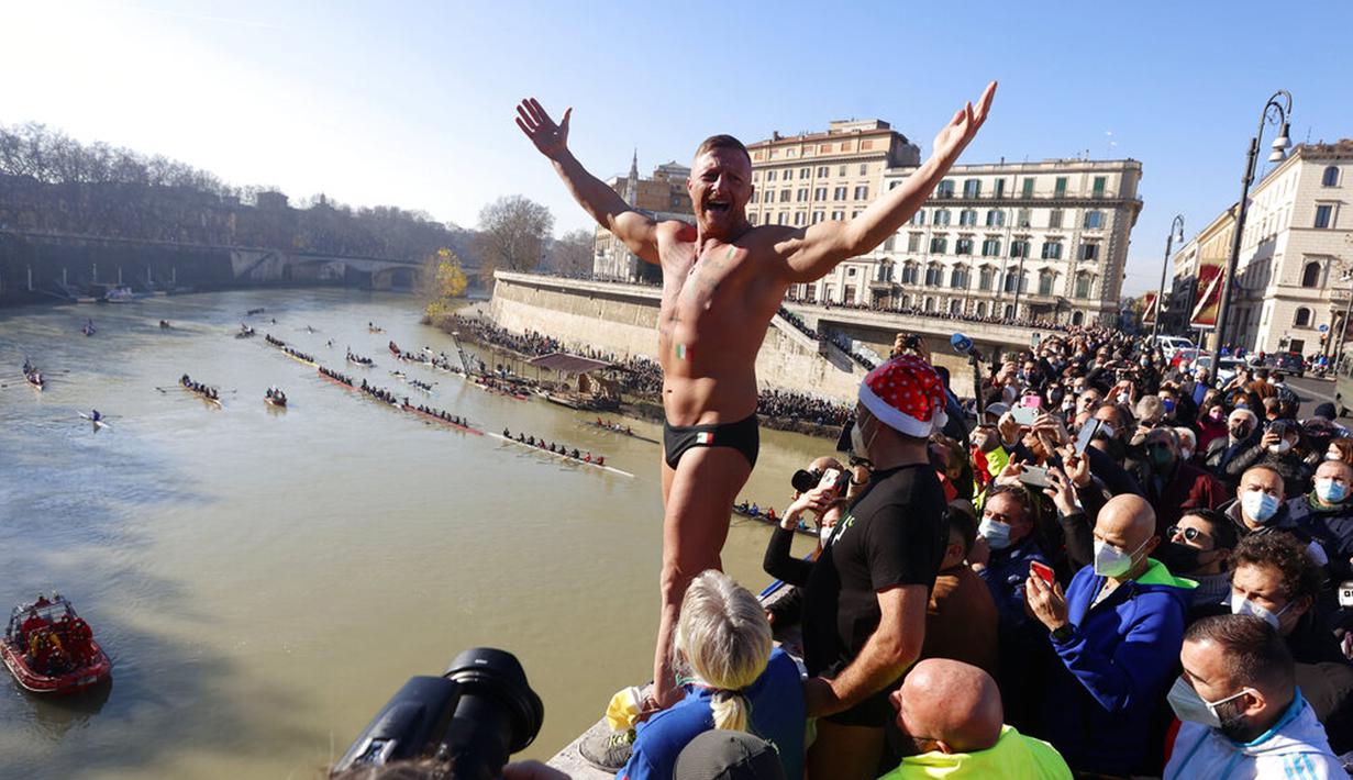 Simone Carabella dari Italia menyapa orang-orang saat dia bersiap untuk melompat ke Sungai Tiber dari Jembatan Cavour setinggi 18 meter (59 kaki) untuk merayakan Tahun Baru di Roma, 1 Januari 2022. (AP Photo/Riccardo De Luca)