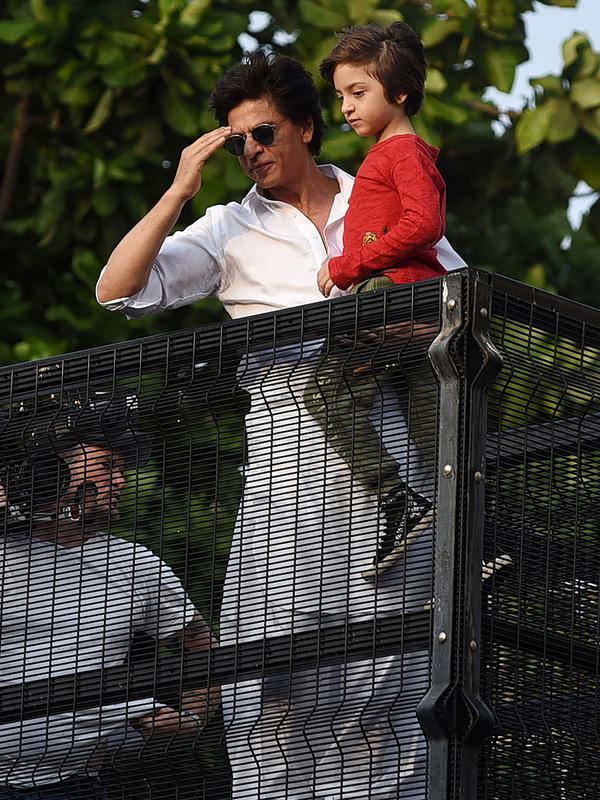 Aktor Bollywood, Shah Rukh Khan menggendong putranya, Abram Khan menyapa para fans yang berkumpul di depan rumahnya pada perayaan Idul Fitri di Mumbai, Rabu (5/6/2019). Ribuan penggemar kerap berkumpul di depan rumah Shah Rukh Khan di momen-momen tertentu. (SUJIT JAISWAL/AFP)