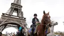 Sejumlah penunggang kuda melintas di depan Menara Eiffel saat mengikuti parade kuda ke-20 di Paris, Prancis (19/11). Acara ini menjadi ajang untuk berkumpul bagi mereka pecinta kuda. (AFP Photo/Thomas Samson)