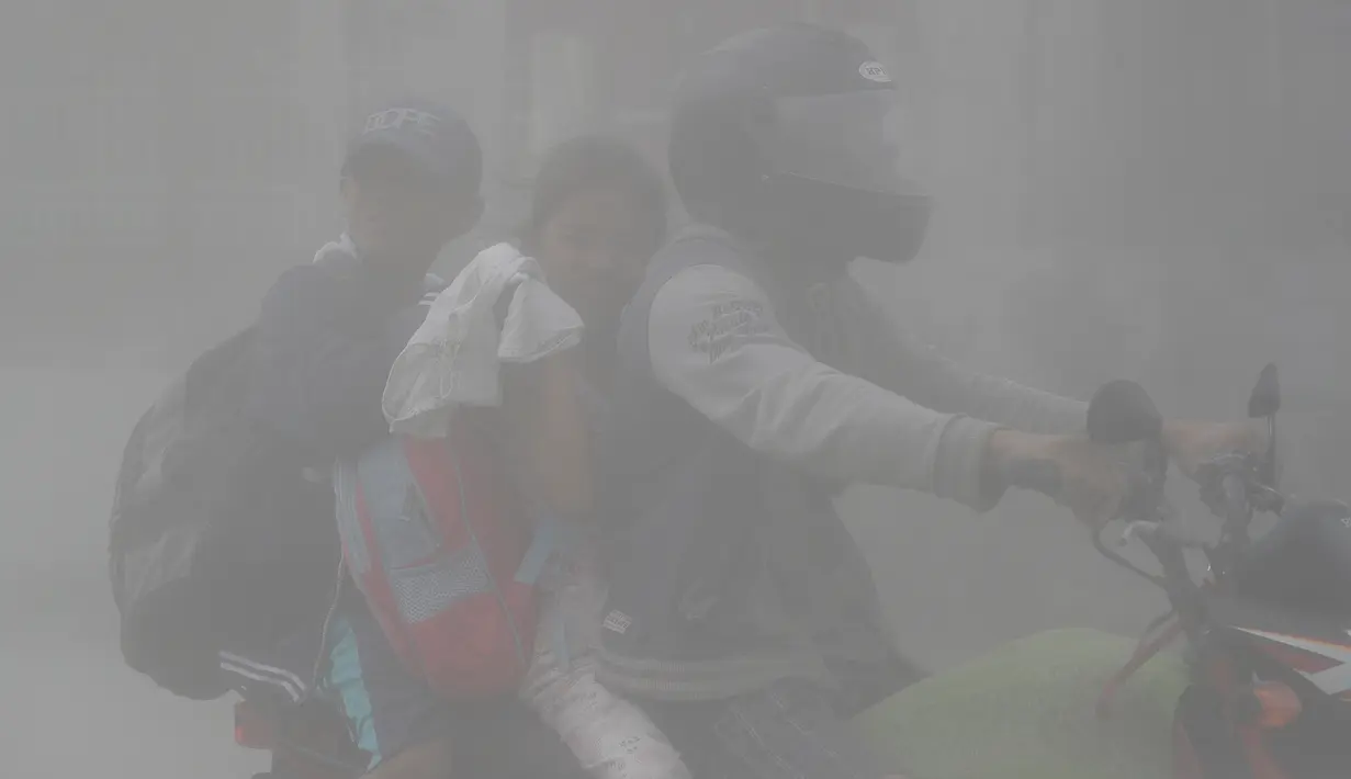 Sebuah keluarga mengendarai motor menembus abu vulkanik gunung Taal untuk mengungsi ke tempat yang lebih aman di Lemery, provinsi Batangas, Filipina, Senin (13/11/2020). Erupsi gunung Taal memaksa puluhan ribu orang mengungsi serta membuat sekolah-sekolah dan toko di Manila tutup. (AP/Aaron Favila)