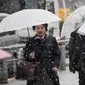 Warga menggunakan payung berjalan selama hujan salju lebat di Tokyo (22/1). Hujan salju membuat keberangkatan penerbangan dan melumpuhkan beberapa layanan kereta api di kota tersebut. (AFP Photo/Behrouz Mehri)