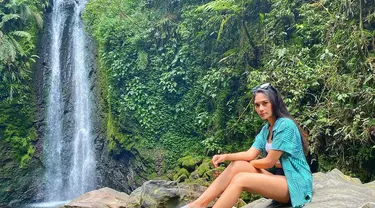 Garneta Haruni nampak santai dengan kemeja biru dan sepatu slip on. Ia nampak sedang menikmati liburannya di sebuah air terjun di daerah Jawa Barat. (Liputan6.com/IG/@garnetaharuni).