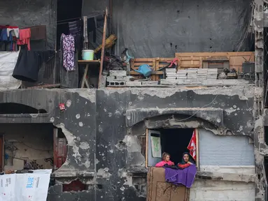 Anak-anak perempuan Palestina yang mengungsi melihat keluar rumah yang rusak tempat mereka berlindung di Beit Lahia di Jalur Gaza utara, menjelang waktu berbuka puasa selama bulan suci Ramadan pada 9 Maret 2025. (Omar AL-QATTAA/AFP)