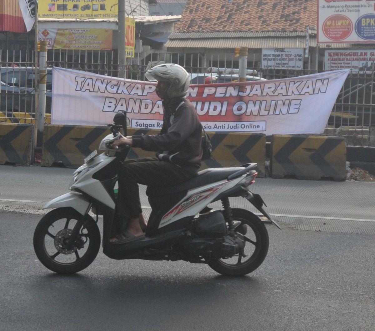 Pengendara melintas di dekat spanduk 'Tangkap dan Penjarakan Bandar Judi Online' yang terpampang di kawasan Mampang, Jakarta, Kamis (1/8/2024). Spanduk tersebut menyuarakan keresahan masyarakat terhadap menjamurnya praktik judi online. Foto: Merdeka.com/I