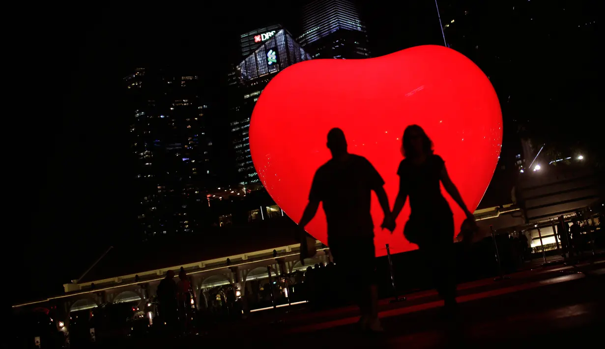 Siluet sepasang pria dan wanita dengan latar belakang balon berbentuk hati saat festival Light Marina Bay di Singapura (8/3). Instalasi seni cahaya ini dirancang dengan pencahayaan ramah lingkungan yang hemat energi. (AP Photo / Wong Maye-E)