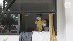 Pasien Covid-19 bersama seorang anak terlihat dari jendela Graha Wisata Ragunan, Jakarta, Selasa (15/6/2021). Pemprov DKI memfungsikan kembali Graha Wisata Ragunan sebagai tempat isolasi warga terpapar COVID-19 kategori OTG sejak pekan lalu dan saat ini merawat 117 pasien. (merdeka.com/Arie Basuki)