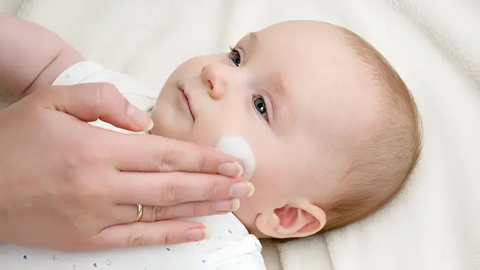 Seorang ibu sedang memberikan krim ke wajah bayinya (Foto Dok: Freepik/artfolio)